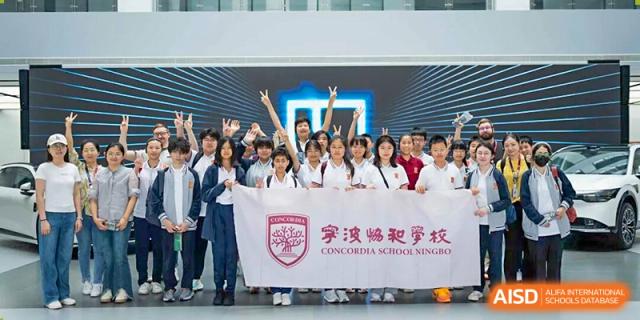 A large group of happy students in uniforms holding a banner with the school logo and Chinese characters, celebrating a group achievement at Concordia International School Ningbo.