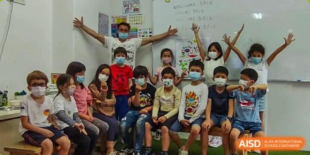 A teacher and a large group of students wearing face masks pose together near a whiteboard in a classroom at École Française Internationale de Shenzhen(EFIS).