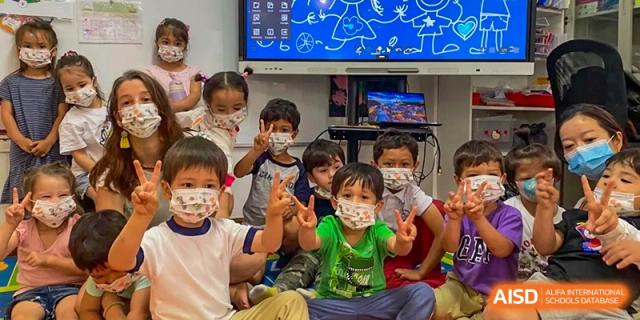 A group of young students wearing face masks pose together in a classroom in front of a digital screen at École Française Internationale de Shenzhen(EFIS).