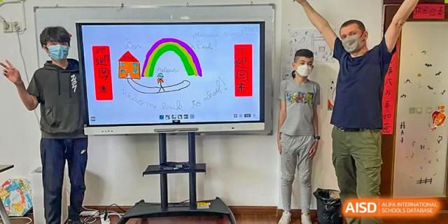 A student stands next to a large interactive digital whiteboard displaying colorful drawings at École Française Internationale de Shenzhen(EFIS).