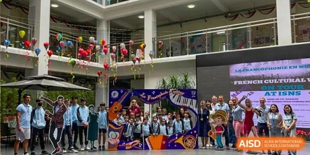 A large group of students and staff pose for a photo in front of a colorful musical-themed backdrop at École Française Internationale de Shenzhen(EFIS).