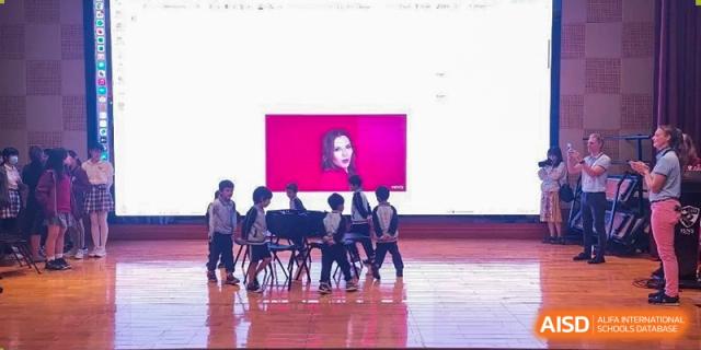Students on a stage looking at a large screen during a presentation or musical performance at École Française Internationale de Shenzhen(EFIS).