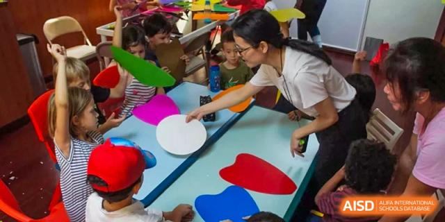 A teacher helps young students with a hands-on craft activity using colorful paper shapes at École Française Internationale de Shenzhen(EFIS).