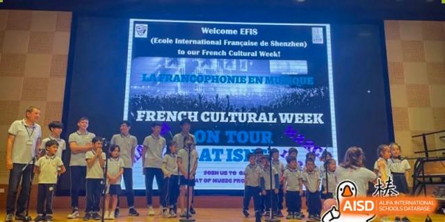 Students perform on a stage in front of a digital screen announcing French Cultural Week and "La Francophonie en Musique" at École Française Internationale de Shenzhen (EFIS).