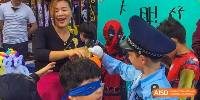 A teacher and students in costumes, including Deadpool and a police officer, interacting during a celebration at École Française Internationale de Shenzhen(EFIS).