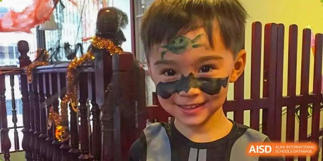 A young boy with green and black superhero face paint smiles for a portrait at École Française Internationale de Shenzhen (EFIS).
