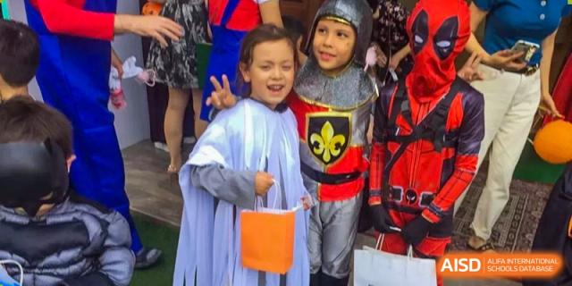 Two children dressed as a knight and a royal pose with an orange treat bag at École Française Internationale de Shenzhen (EFIS).