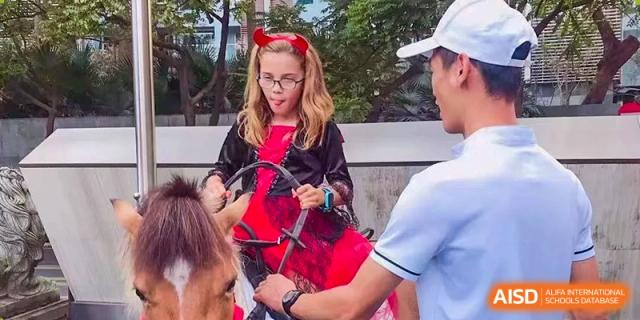 A student in a red and black devil costume sits on a pony during a school fair at École Française Internationale de Shenzhen(EFIS).