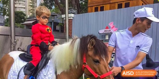 A boy in a superhero costume rides a pony guided by an adult during an event at École Française Internationale de Shenzhen(EFIS).