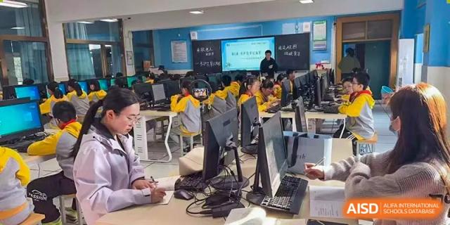 Students are working on computers in a modern lab, concentrating on their screens while supervised by a teacher in the background during a technology class at Hefei Xinhua Academy.