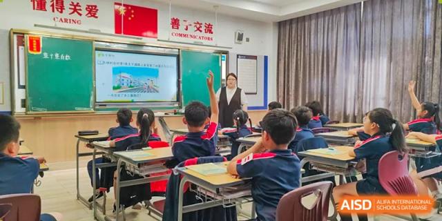 A teacher is leading a lesson, pointing at an interactive smart board while students are sitting attentively in their desks and participating in the class at Hefei Xinhua Academy.