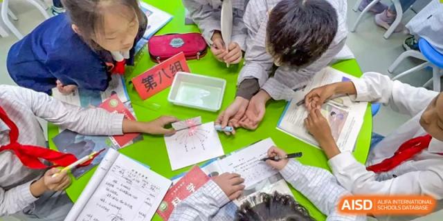 An overhead view of a small group of students collaborating and writing on green paper during a focused group study or workshop session at Hefei Xinhua Academy.