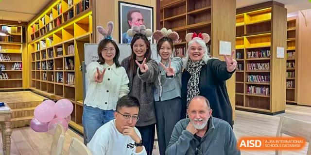 A group of adults, including both staff and visitors, posing for a friendly photo together inside the school premises, Hefei Xinhua Academy.