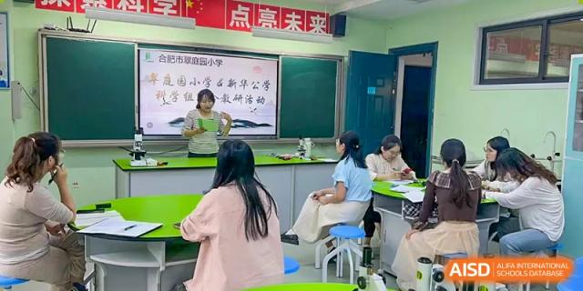 A teacher instructing a small group of students sitting at desks in a classroom with a presentation on the blackboard, Hefei Xinhua Academy.