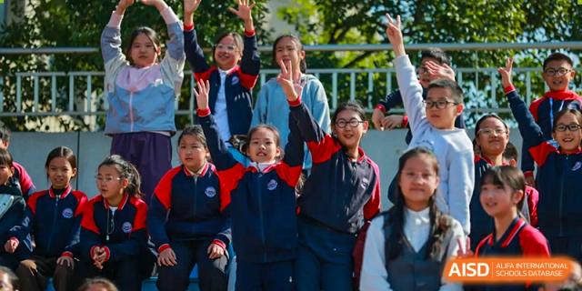 A group of energetic students in school uniforms smiling and waving their hands outdoors in a joyful manner, Hefei Xinhua Academy.