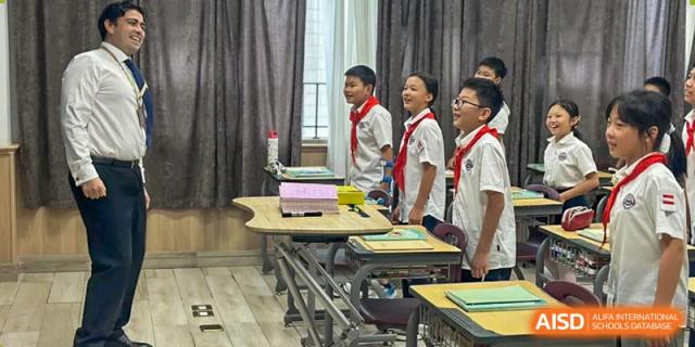 Students in school uniforms standing together, smiling and looking forward in a classroom setting with empty desks, Hefei Xinhua Academy.