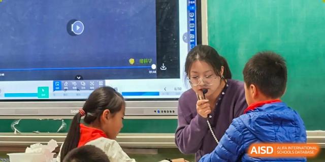 A student holds a microphone and speaks while a teacher listens during an interactive lesson using a digital screen, Hefei Xinhua Academy.