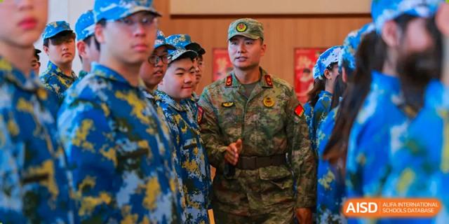 A military officer in camouflage uniform standing with several students/cadets in blue and green uniforms, possibly during a training or official event at Hefei Xinhua Academy.