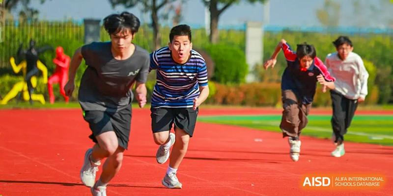 An energetic male student, dressed in athletic gear, is captured running at full speed on the vibrant red track during a race, concentrating intensely on the finish line in the outdoor sports complex of Hefei Xinhua Academy.