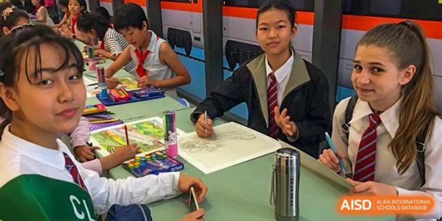 A student from Pakistan Embassy College Beijing working on an art project with paper and crayons in a classroom setting.