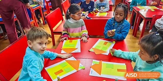 Students from Pakistan Embassy College Beijing working collaboratively on a colorful paper-based project at a red table.