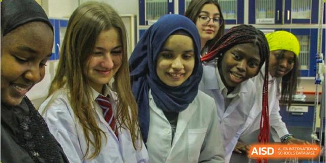 A female student from Pakistan Embassy College Beijing wearing a hijab and lab coat, smiling with her classmates.