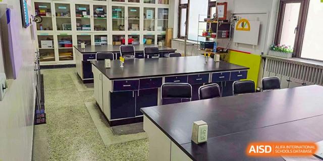 An empty science lab or classroom at Pakistan Embassy College Beijing with large wooden tables and dark storage units.