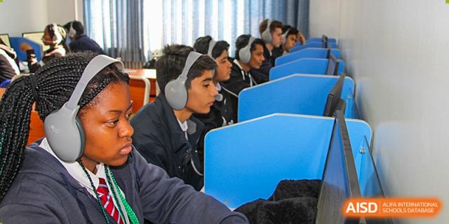 Students from Pakistan Embassy College Beijing working on desktop computers in a dedicated computer lab with blue partitions.