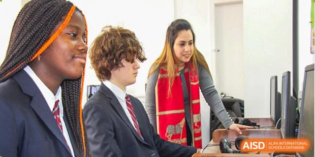 A teacher guiding a male student from Pakistan Embassy College Beijing who is working on a task at a desk.