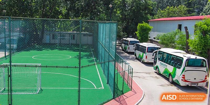 An outdoor sports court area next to a row of buses, likely the transport fleet for Pakistan Embassy College Beijing.
