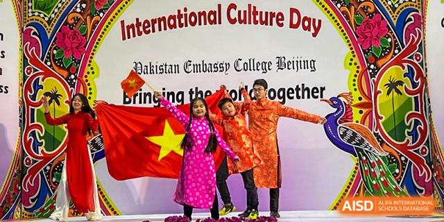 Three students from Pakistan Embassy College Beijing in colorful traditional clothing holding the Vietnamese flag at 'International Culture Day'.