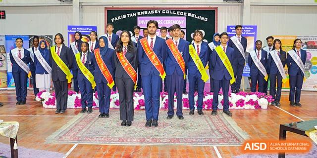 Graduating students from Pakistan Embassy College Beijing in formal attire, wearing sashes, standing together indoors.
