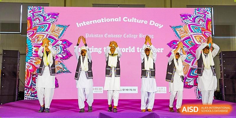 Three male students from Pakistan Embassy College Beijing performing a traditional dance in white attire on stage.