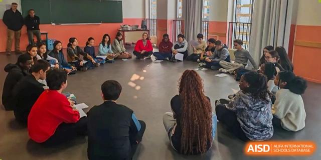 Students at the Proviseur, du Lycée Français International de Pékin, are sitting in a circle on the floor, facing inward for a collaborative group discussion or activity session.