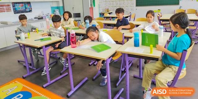A student from the Proviseur, du Lycée Français International de Pékin, is focused on writing at their desk in a classroom setting with a tablet and books nearby.