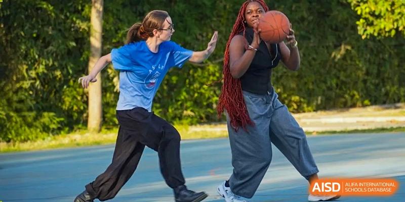 Two people facing each other on an outdoor court, one attempting to guard the other who is holding a basketball. Proviseur, du Lycée Français International de Pékin.