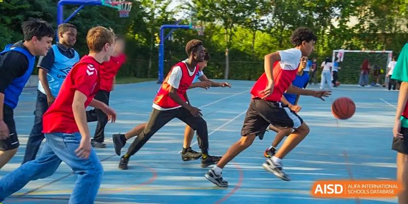 A group of boys in red and black athletic gear running quickly during an outdoor sports activity on a blue court. Proviseur, du Lycée Français International de Pékin.