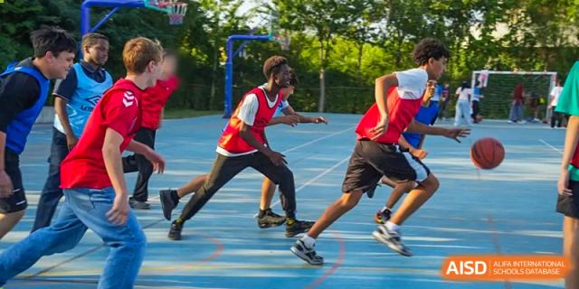 A group of boys in red and black athletic gear running quickly during an outdoor sports activity on a blue court. Proviseur, du Lycée Français International de Pékin.