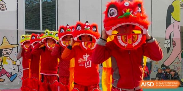 A close-up of children in red performing a Lion Dance, with one holding the colorful lion head during a cultural celebration. Proviseur, du Lycée Français International de Pékin.