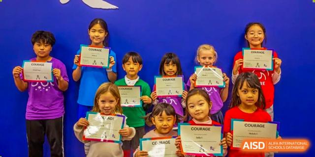 A group of primary students proudly display their "Courage" certificates against a blue background at Tianjin International School (TIS).
