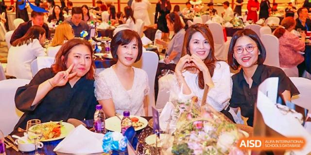 Two women smiling at a formal dinner event with floral arrangements and table settings in the background at Tianjin International School (TIS).