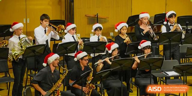 A student band performing in a holiday concert, featuring woodwind players wearing festive red and white Santa hats at Tianjin International School (TIS).