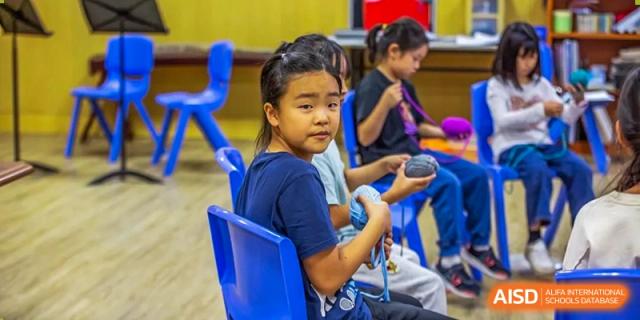 A young student sitting at a blue desk and holding a ball of yarn during a creative hands-on craft session at Tianjin International School (TIS).