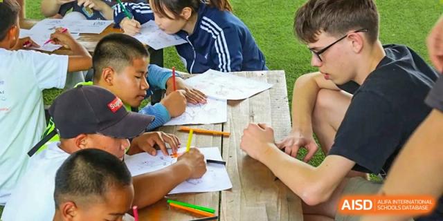 A group of students sitting together at a wooden table, focused on drawing and coloring with vibrant markers at Tianjin International School (TIS).