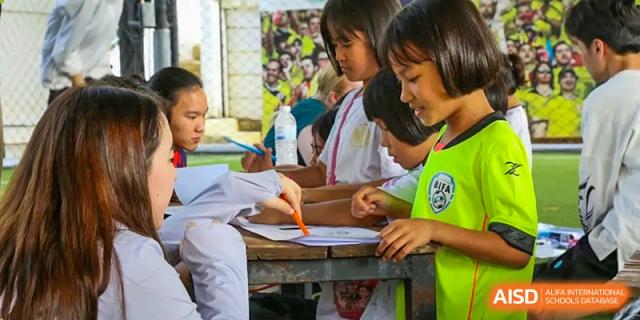 Students working collaboratively on a writing project at an outdoor table during a community event at Tianjin International School (TIS).