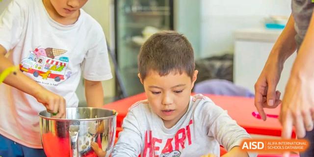 A young boy wearing a "HEART" shirt focuses intently on a classroom activity involving small objects at Tianjin International School (TIS).