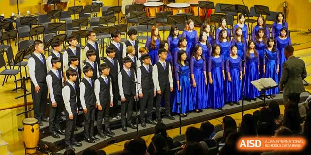 A formal student choir dressed in black vests and blue gowns performs on stage during a concert at Tianjin International School (TIS).