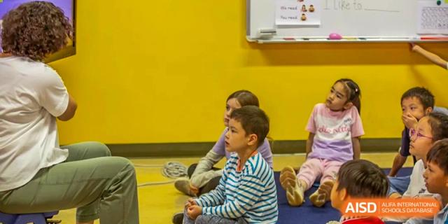 Two young students sit attentively on the floor during a classroom presentation or storytime session at Tianjin International School (TIS).