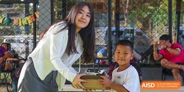 A smiling older student assists a younger child with a project or gift during a community event at Tianjin International School (TIS).