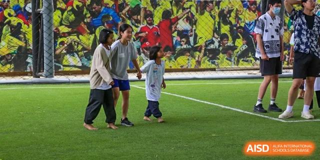 Three young students walking together and holding hands on a green sports field during an outdoor activity at Tianjin International School (TIS).